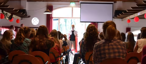 Volle zaal deelnemers kijkt naar een presentatie op het scherm