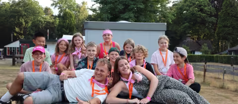 Kinderen en leiding lachen samen rond een tafeltennistafel op kamp