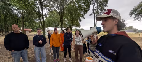 Kampleider spreekt vrijwilligers toe met megafoon op het kampterrein