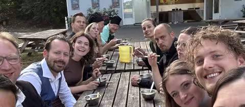 Kampleiding geniet samen van soep aan een lange picknicktafel