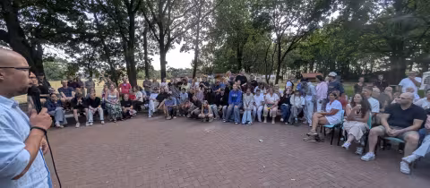 Grote groep tieners en ouders luistert buiten naar de spreker