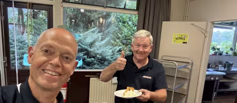 Twee kampvrijwilligers genieten lachend van appeltaart met slagroom.