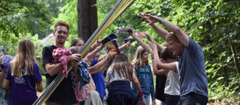 Deelnemers spelen een spel met lange stokken op een open plek in het bos