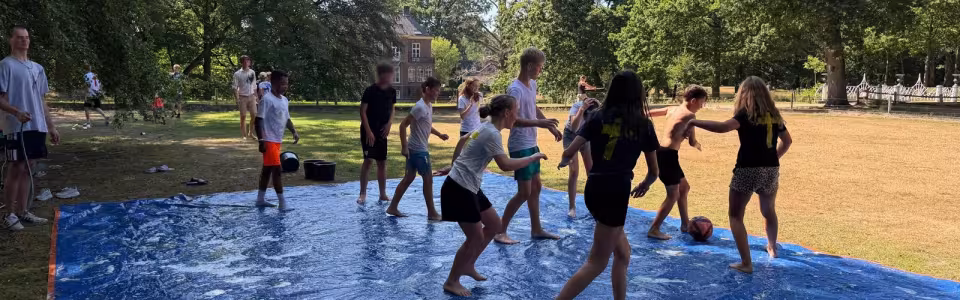 Deelnemers spelen op een nat zeil met glijbaan