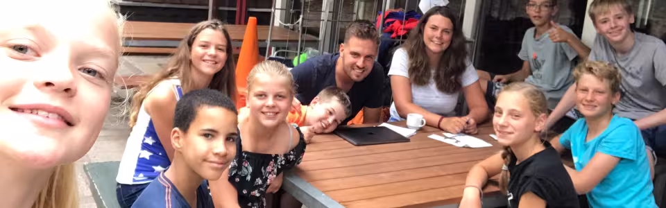 Deelnemers met feestmutsen aan tafel bij het kampgebouw