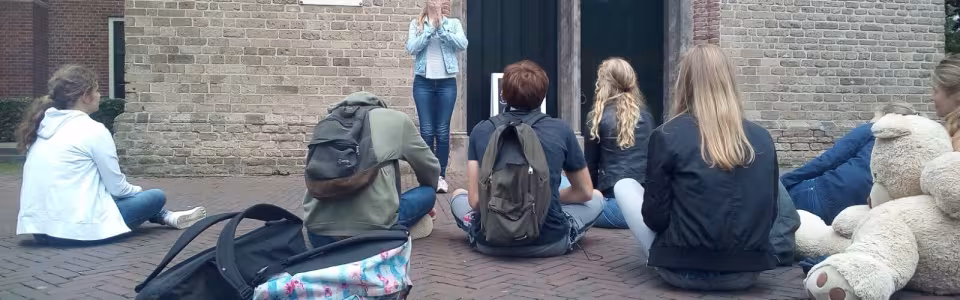 Deelnemers zitten met bagage tegen de muur van het gebouw
