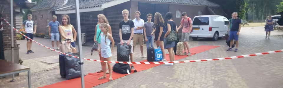 Deelnemers met bagage lopen over een rode loper