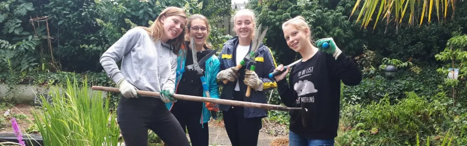 Vier tienermeiden poseren lachend met tuingereedschap in een tuin