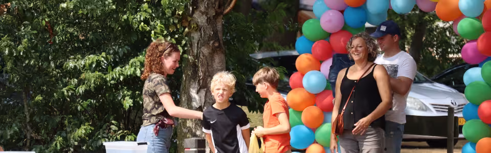 Kinderen arriveren met hun ouders onder een vrolijke ballonnenboog