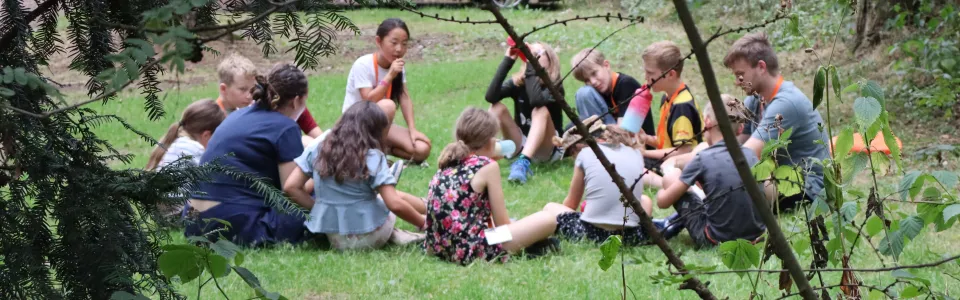 Kinderen en leiding zitten samen in een kring in het bos