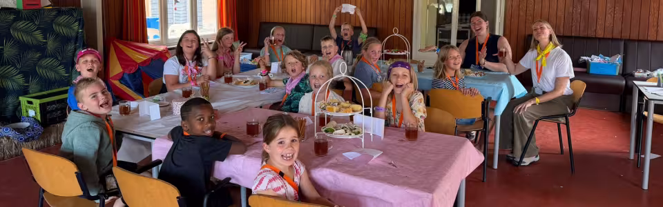 Lachende kinderen en leiding genieten samen van een feestelijke maaltijd.