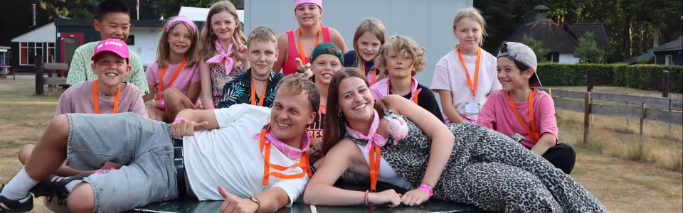 Kinderen en leiding lachen samen rond een tafeltennistafel op kamp