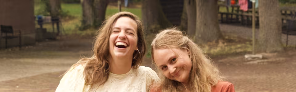 Twee jonge vrouwen lachen samen op het bosrijke kampterrein.