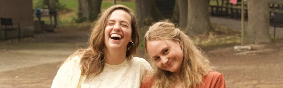Twee jonge vrouwen lachen samen op het bosrijke kampterrein.