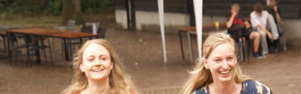 Twee lachende vrouwen lopen samen over het zonnige kampterrein