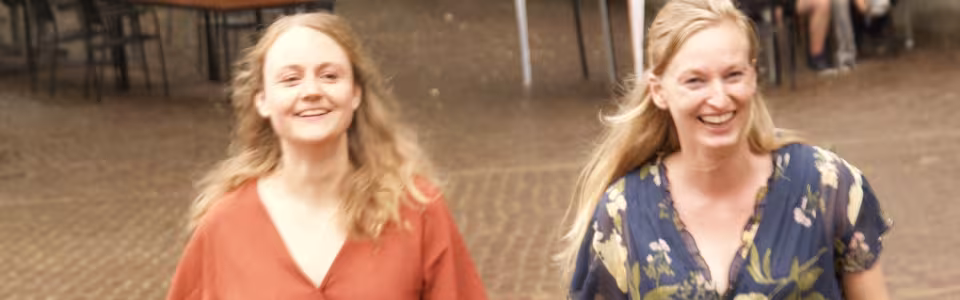 Twee lachende vrouwen lopen samen over het zonnige kampterrein