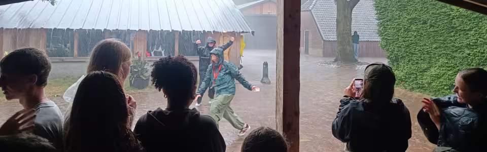Kampleiding danst door de stortregen terwijl tieners beschut juichen