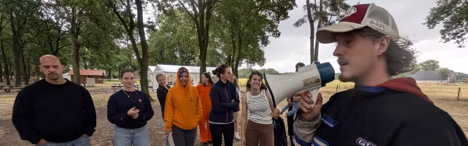 Kampleider spreekt vrijwilligers toe met megafoon op het kampterrein