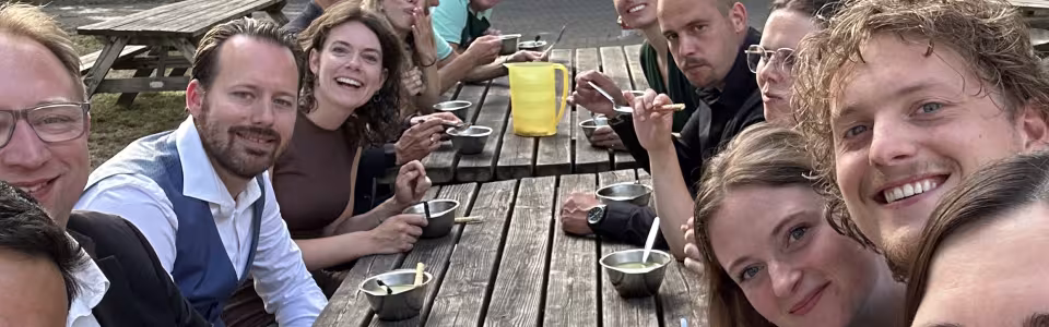 Kampleiding geniet samen van soep aan een lange picknicktafel