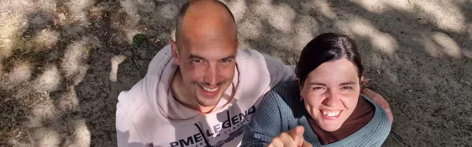 Twee kampleiders kijken lachend omhoog, één wijst naar de camera