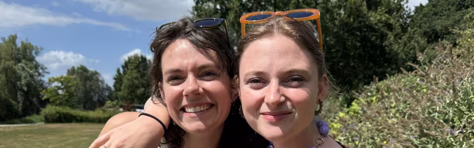 Twee lachende kampleidsters delen snoepjes in de zon.