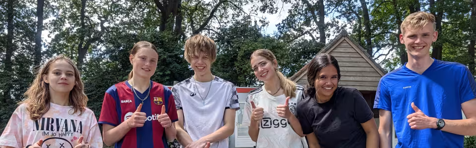 Zes tieners steken samen lachend hun duimen op tijdens jeugdkamp