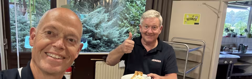 Twee kampvrijwilligers genieten lachend van appeltaart met slagroom.