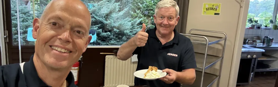 Twee kampvrijwilligers genieten lachend van appeltaart met slagroom.
