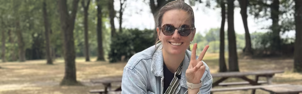 Glimlachende kampleidster maakt vredesteken aan een picknicktafel in het bos