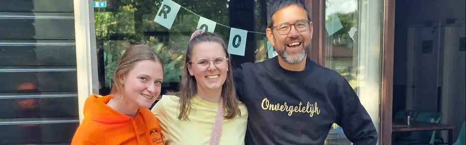 Drie glimlachende kampbegeleiders poseren samen voor het kamphuis