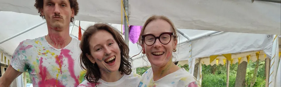 Drie lachende begeleiders poseren samen na een kleurrijk verfspel