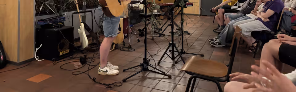 Tieners luisteren aandachtig naar een gitarist tijdens een kampoptreden