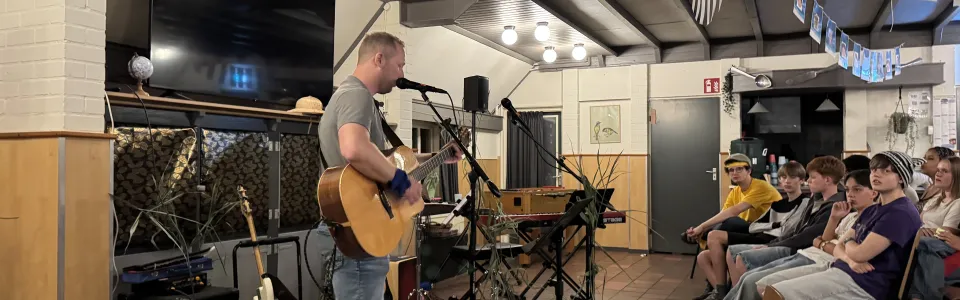 Tieners luisteren aandachtig naar een gitarist tijdens een kampoptreden