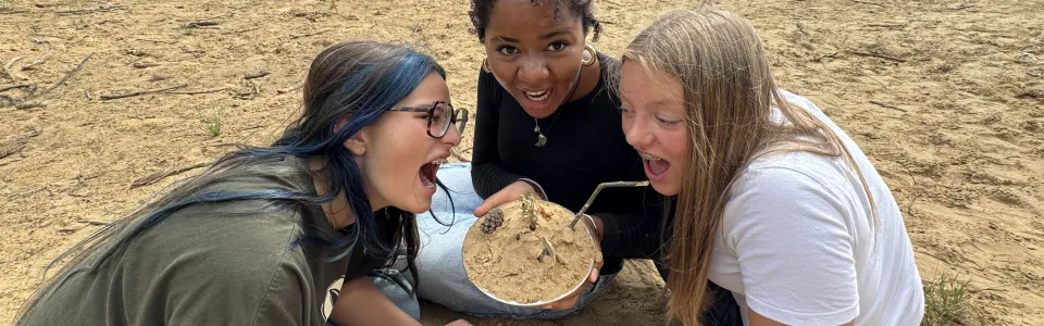 Drie tieners bewonderen enthousiast hun zandcreatie in de natuur
