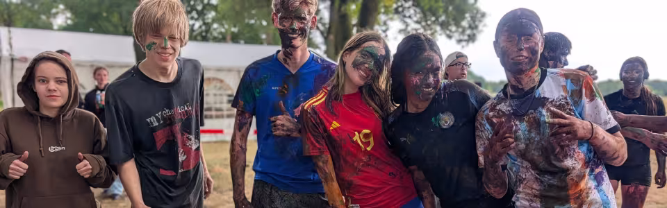 Tieners poseren lachend na een kleurrijk moddergevecht op kamp