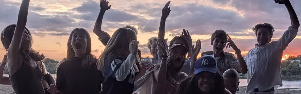 Juichende tieners springen samen op tijdens een kleurrijke zonsondergang