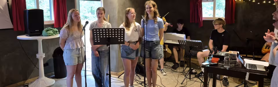 Tieners zingen samen terwijl muzikanten hen begeleiden tijdens het jeugdkamp
