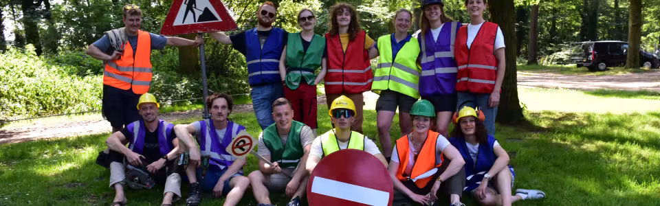 Kampleiding poseert vrolijk in verkeershesjes en bouwhelmen in het bos.