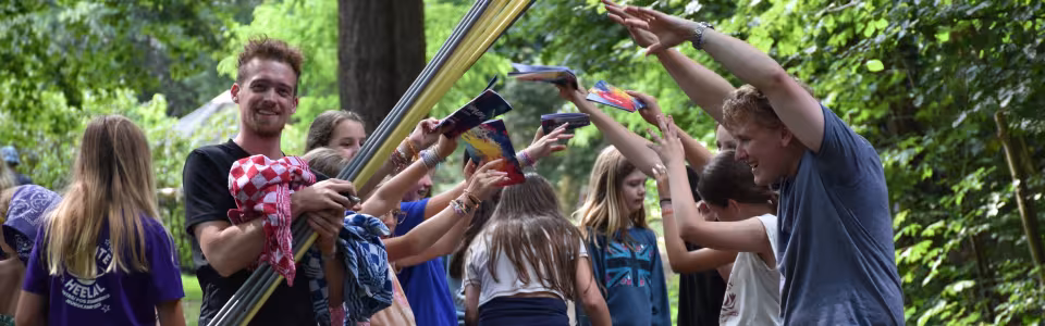 Deelnemers spelen een spel met lange stokken op een open plek in het bos