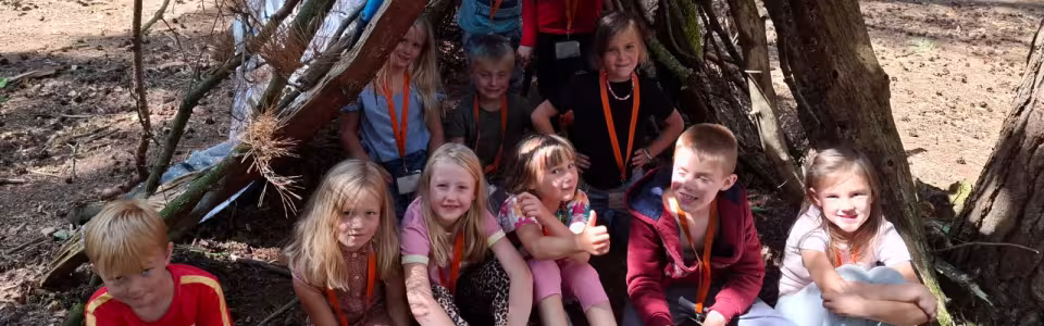 Kinderen poseren trots bij hun zelfgebouwde boshut tijdens kamp.