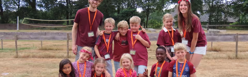 Kampleiders poseren lachend met hun groep kinderen op het veld