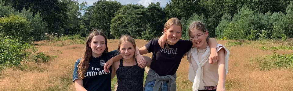 Vier tienermeiden lopen arm in arm over een zandpad