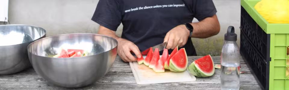 Kampleider snijdt verse watermeloen in stukken aan de buitentafel