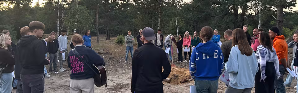 Tieners zingen samen in een kring tijdens een bosavond.
