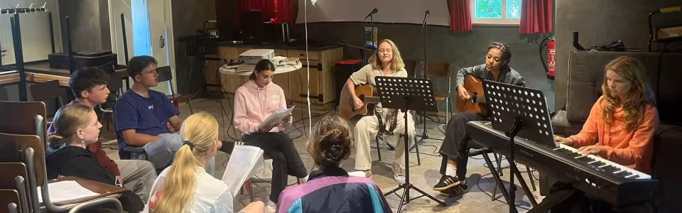 Tieners zingen samen met gitaren en piano in de kampzaal