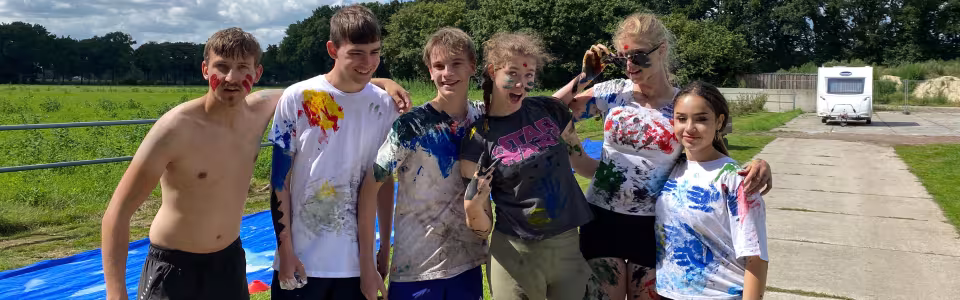 Tieners poseren lachend na een kleurrijk verfspel op kamp