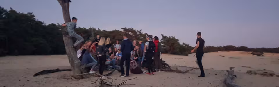 Deelnemers bij een kale boom op de zandvlakte in de avond