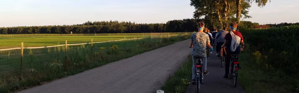 Deelnemers lopen en fietsen over een landweg bij zonsondergang