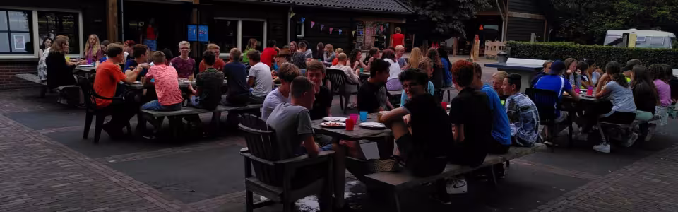 Deelnemers aan picknicktafels bij het kampgebouw