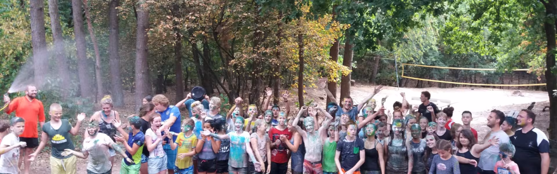 Grote groep deelnemers op het kampterrein tussen de bomen